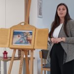 Povečan pogled na pripovedovalko, ki stoji ob kamišibaj stojalu. V okvirju stojala je ilustracija zimskega prizora z živalmi.