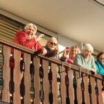 Več oseb stoji na balkonu stavbe in maha navzdol proti dogajanju pred stavbo.