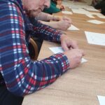 Oseba sedi za mizo in piše na list papirja, na mizi so razporejeni listi z narisanimi srci.