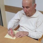 Stanovalec doma za starejše piše novoletno željo na list papirja v skupnem prostoru.