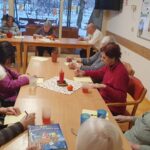 Stanovalci doma za starejše sedijo za mizo in skupaj pišejo novoletne želje v dnevnem prostoru.