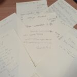 Na mizi so razporejeni listi papirja z ročno napisanimi novoletnimi željami.