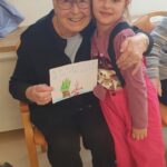 Starejša oseba in otrok sedita skupaj, starejša oseba drži risbo, otrok je objemajoče ob njej.