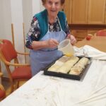 Stanovalka premaže zavitek z maščobo na pekaču pred peko.