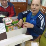 Stanovalca ob ogledu vsebine darilne škatle, ob tem pa dobra volja in sproščeno praznično vzdušje.