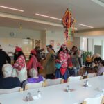 Osebe v kostumih hodijo skozi jedilnico, kjer druge osebe sedijo ob mizah in jih opazujejo.