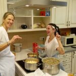 Dve ženski v kuhinji stojita ob štedilniku z lonci hrane in držita kuhalnico.