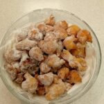 Steklena posoda je napolnjena z ocvrtim pecivom, posutim s sladkorjem v prahu.