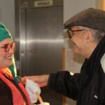 Dve osebi se nasmejani pogovarjata in se dotakneta rok v hodniku ob dvigalu.