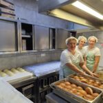 Tri osebe stojijo v kuhinji ob delovni mizi s pladnji krofov in pozirajo ob pripravljeni hrani.