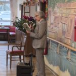 Oseba stoji ob steni, bere iz knjige in govori v mikrofon.