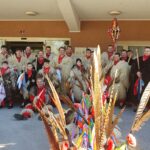 Skupina kurentov in zaposlenih stoji pred vhodom doma; v ospredju so pisani trakovi in perje.