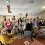 Skupinska fotografija kurentov in drugih pustnih mask skupaj s stanovalci v skupnem prostoru doma.