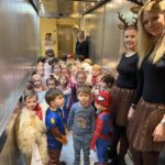 Več otrok v pustnih kostumih in dve odrasli osebi stojijo v dvigalu in gledajo proti fotoaparatu.