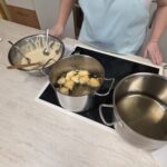 Oseba stoji ob štedilniku z lonci vročega olja in posodo z zmesjo za cvrtje.