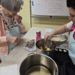 Dve osebi stojita ob štedilniku in s penovko pobirata ocvrto pecivo iz lonca.