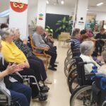 Starejši obiskovalci sedijo v prostoru in ploskajo po koncu nastopa.