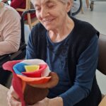 Oseba sedi in v rokah drži barvno papirnato rožo, na mizi sta vrvica in telefon.