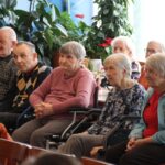 Skupina starejših oseb sedi na stolih in posluša dogajanje v prostoru.