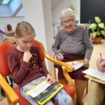 Deklica in starejša ženska sedita na stolih ter izpolnjujeta liste s številkami.