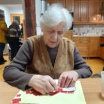 Ženska sedi za mizo in na papir lepi majhne rdeče koščke v obliki srca.