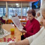 Ženska za mizo drži list z narisanim motivom src in rož ter svinčnik v roki.