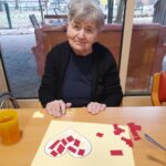 Ženska sedi za mizo, pred njo je list s srcem iz lepljenih rdečih koščkov papirja.