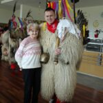 Oseba v kosmatem pustnem kostumu stoji ob drugi osebi, ki stoji ob njej v notranjem prostoru.