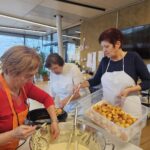 Tri osebe v predpasnikih pripravljajo ocvrto testo nad posodo z oljem in mešajo maso v veliki skledi.