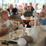 Stanovalke skupaj barvajo buče z belo barvo in jih pripravljajo za nadaljnje okraševanje. Delajo z rokavicami in čopiči, zelo zbrano in natančno.