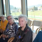 Štiri ženske sedijo na stolih ob oknu v notranjem prostoru.