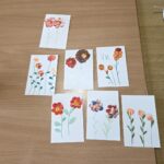 Na mizi so razporejeni končani likovni izdelki z naslikanimi cvetovi.