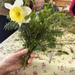 Roka drži šopek iz zelenja in rumenega cveta, povezan z vrvico.