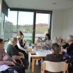 Mlajši in starejši skupaj sedijo za mizo ter izdelujejo barvne okraske.