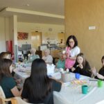 Skupina sedi za mizo, kjer skupaj ustvarjajo velikonočne okraske pod vodstvom zaposlene.