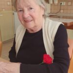 Ženska sedi za mizo in drži rdeč nagelj v roki.