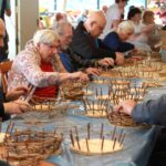 Stanovalci in stanovalke skupaj izdelujejo košarice iz vejic. Vsak ima pred seboj leseno osnovo, okoli katere prepletajo tanke veje.