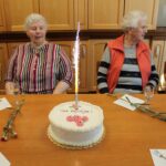 Oseba igra harmoniko, medtem ko druge osebe sedijo za mizo in ploskajo.