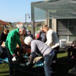 Več oseb na prostem skupaj nasipa zemljo v samokolnico in korito za sajenje.