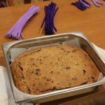 Pečen kruh je položen v kovinskem pekaču na mizi, okoli njega je pripravljeno ustvarjalno gradivo.