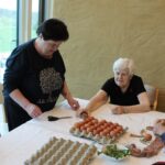 Stanovalke pripravljajo jajca za barvanje, pri tem pa uporabljajo naravne materiale in skrbno zavijajo pirhe.