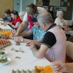 Stanovalci ob pomoči zaposlenih sodelujejo pri ustvarjanju pirhov, kjer skupaj zavijajo jajca in pripravljajo okraske.
