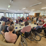 Prostor je poln stanovalcev, zaposlenih in dijakov, ki skupaj ustvarjajo in barvajo pirhe v prijetnem, družabnem vzdušju.