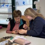 Stanovalka in dijakinja skupaj pripravljata jajce za barvanje, pri čemer dijakinja pomaga in razlaga postopek.