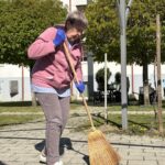 Oseba z metlo pometa tlakovano površino na prostem.