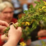 Roke osebe povezujejo šopek iz vejic in cvetov z vrvico.