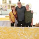 Tri osebe stojijo za mizo, prekrito s sveže narezanimi rezanci, in pozirajo za fotografijo.