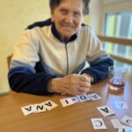 Oseba sedi za mizo in sestavlja besedo iz kartic s črkami.