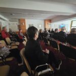 Še en pogled na občinstvo med filmsko projekcijo, kjer starejši sproščeno sedijo in uživajo v ogledu.