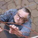 Moški stoji pod trto in z rokami ureja oziroma pregleduje njene poganjke.